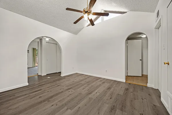 an empty room with wooden floor ceiling fan and windows