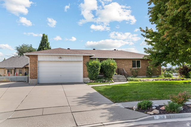 328 Heather Ridge Circle Sandy, UT 84070 - Photo 2 of 28 Brick exterior residence featuring an attached garage with a concrete driveway, a manicured front lawn, mature trees, and tiered concrete steps leading to the entrance