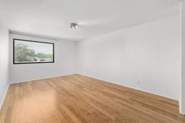 a view of empty room with wooden floor and kitchen