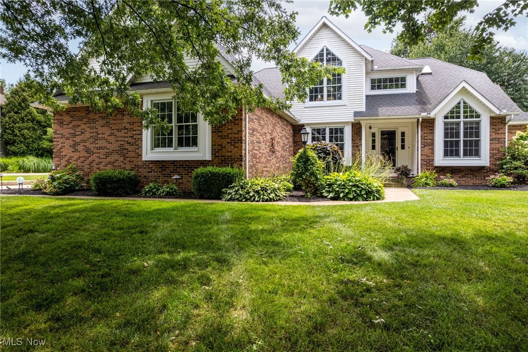 View of front of house featuring brick siding, a front yard, and roof with shingles