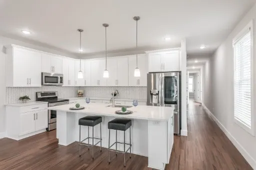 a kitchen with stainless steel appliances kitchen island a refrigerator a stove a sink and a dining table with wooden floor