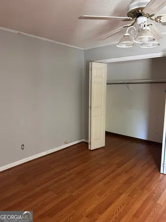 a view of an empty room with wooden floor and a ceiling fan