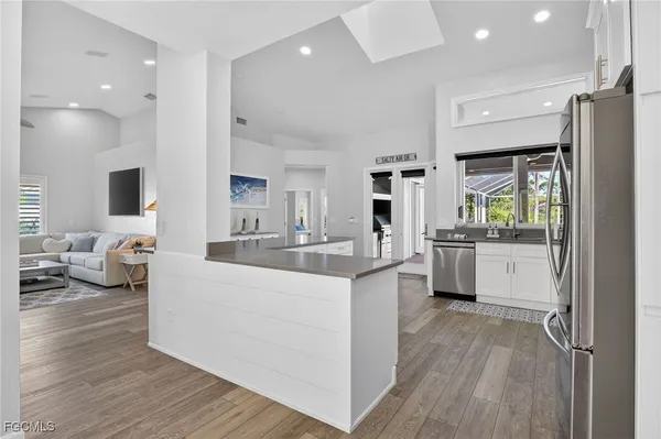 a large white kitchen with a stove a sink dishwasher and a refrigerator with wooden floor