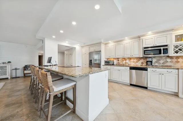 a kitchen with stainless steel appliances granite countertop a stove top oven a sink a refrigerator and white cabinets