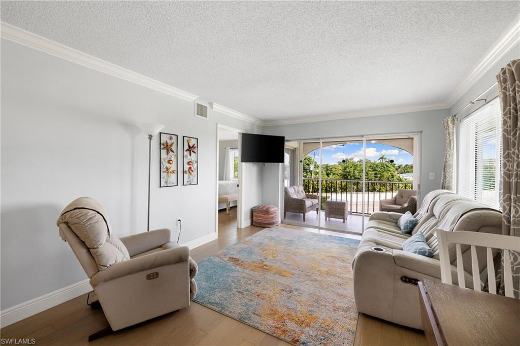 5 High Point Circle West, Unit 307 Naples, FL 34103 - Photo 7 of 31 Living room featuring wood finished floors, ornamental molding, and a textured ceiling