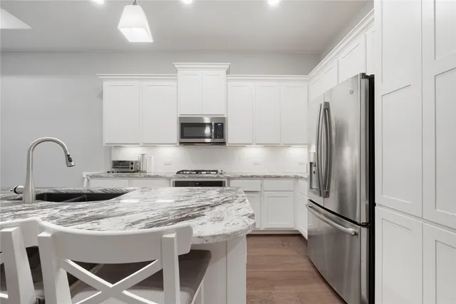 a kitchen with stainless steel appliances granite countertop a refrigerator a stove a sink and white cabinets