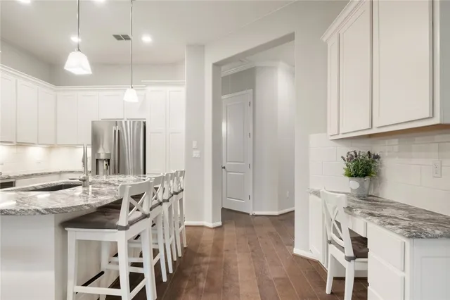 a kitchen with stainless steel appliances granite countertop a stove top oven a refrigerator a sink and white cabinets with wooden floor