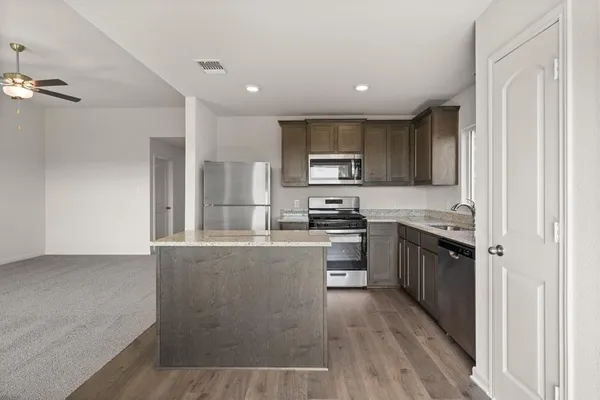 a kitchen with stainless steel appliances granite countertop a refrigerator a stove top oven a sink and dishwasher with wooden floor