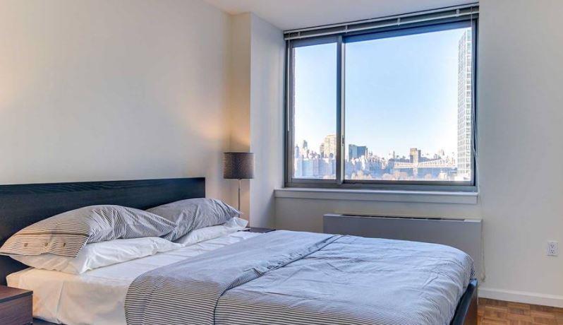 4-75 48th Avenue, Unit 1502 Queens, NY 11109 - Photo 4 of 12 a bedroom with a large bed and a large window