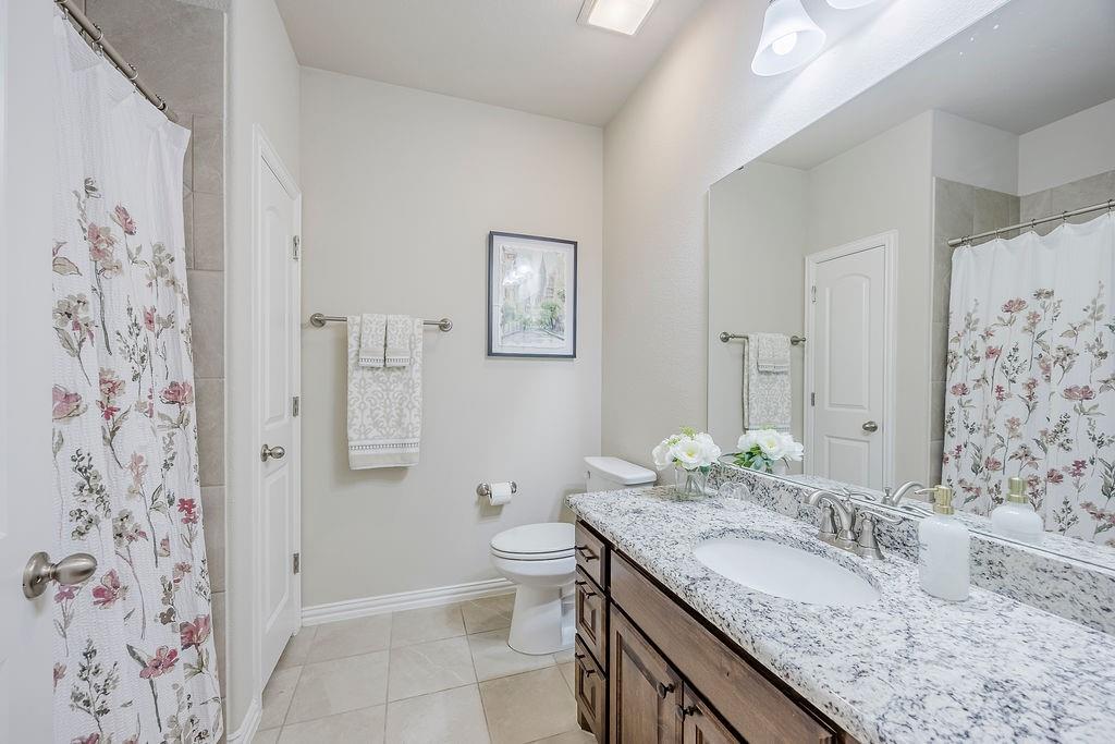 2123 Ladera Way, Unit 2123 Mansfield, TX 76063 - Photo 28 of 34 a bathroom with a granite countertop sink a toilet and shower curtain