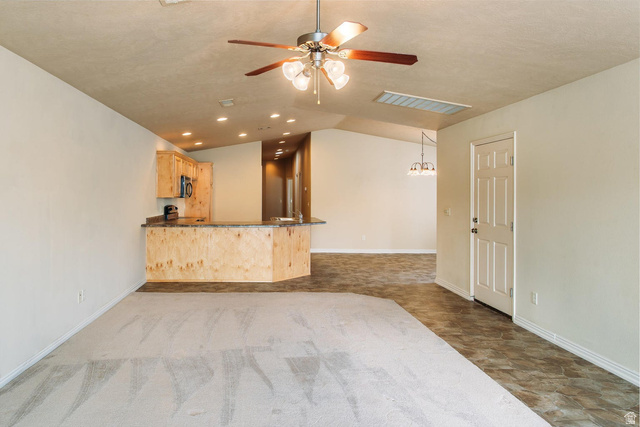 1330 North Dixie Downs Road, Unit 72 St. George, UT 84770 - Photo 4 of 21 Unfurnished living room with ceiling fan, dark colored carpet, hanging lights, stone finish floors, and vaulted ceiling
