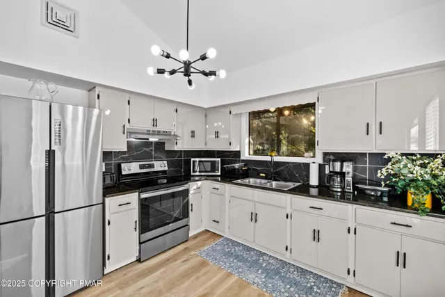 a kitchen with stainless steel appliances a sink a stove a refrigerator cabinets and a window