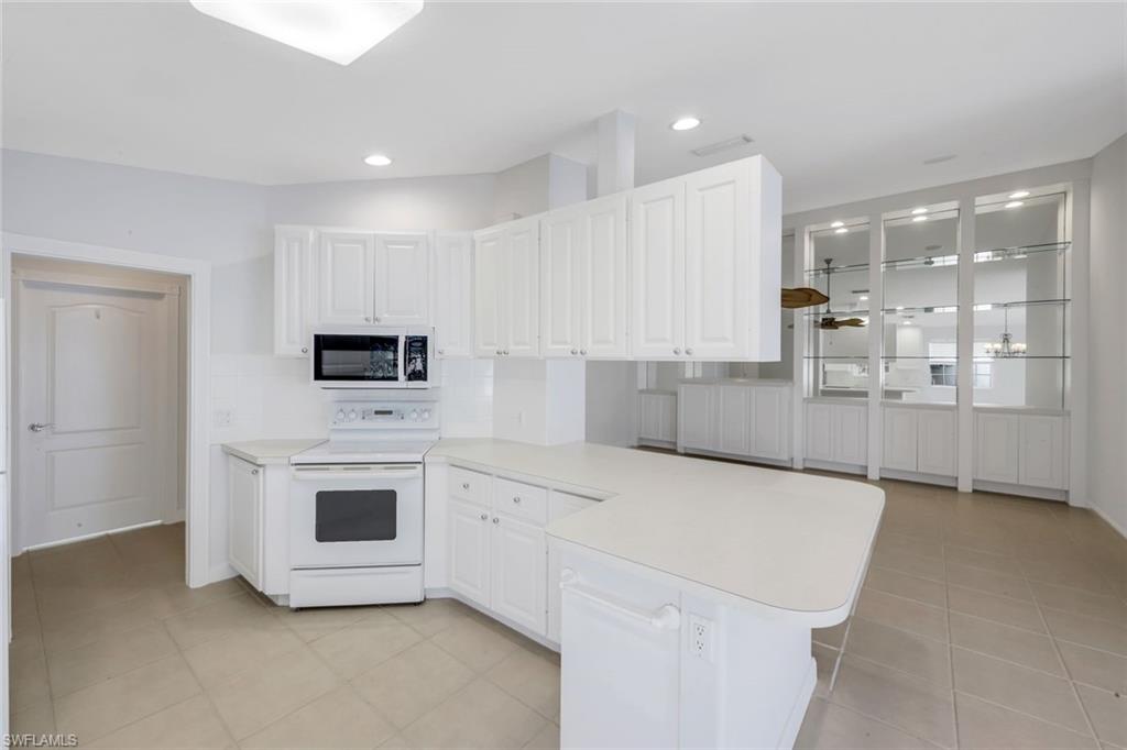 3748 Exuma Way Naples, FL 34119 - Photo 26 of 50 Kitchen featuring white range with electric cooktop, light countertops, a peninsula, white cabinets, and light tile patterned floors