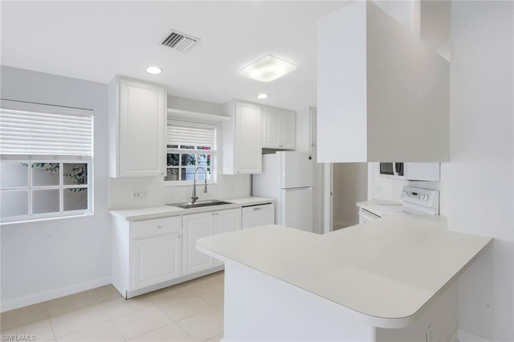 3748 Exuma Way Naples, FL 34119 - Photo 30 of 50 Kitchen with a peninsula, white appliances, light countertops, white cabinetry, and recessed lighting