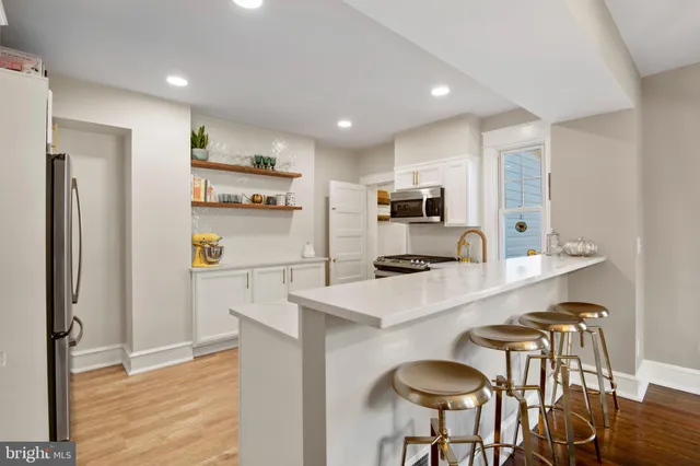 a kitchen with stainless steel appliances a refrigerator a sink a stove a dining table and chairs with wooden floor