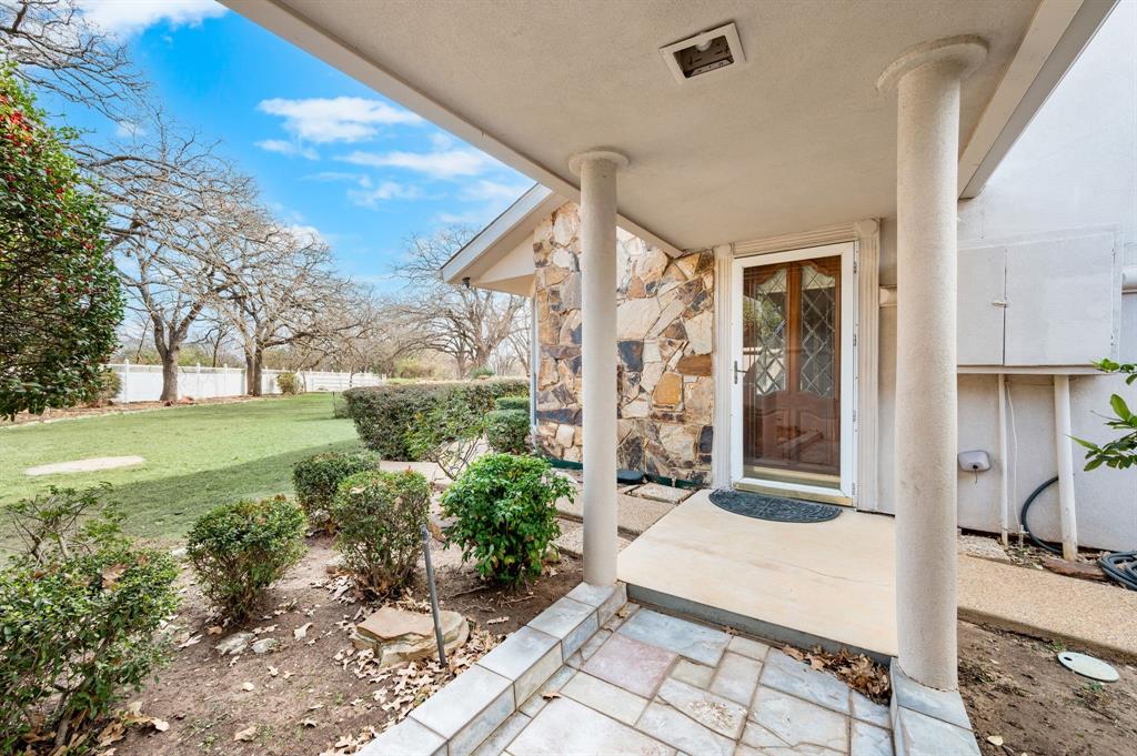 7260 Hudson Cemetery Road Mansfield, TX 76063 - Photo 31 of 40 Stone accent wall entrance featuring a covered porch with round columns, a decorative wood-panel door, and tiled entry