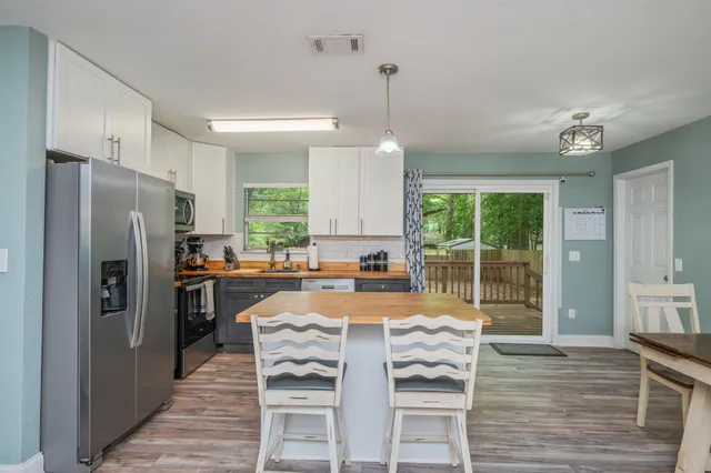 a kitchen with granite countertop a refrigerator a stove a oven and white cabinets with wooden floors