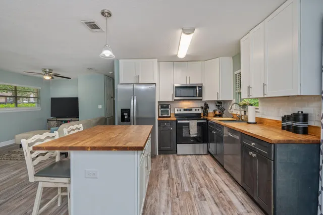 a kitchen with stainless steel appliances granite countertop a refrigerator a stove top oven a sink dishwasher and white cabinets with wooden floor