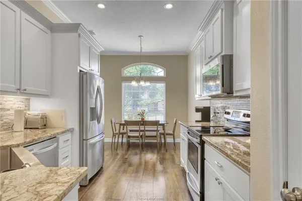 a kitchen with stainless steel appliances a stove a sink dishwasher a refrigerator white cabinets and wooden floor next to a window