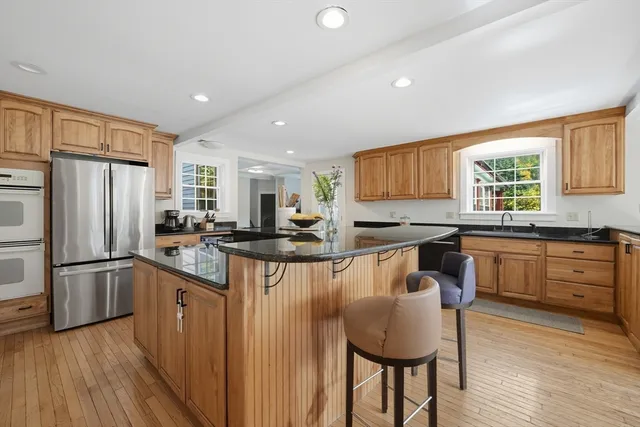 a kitchen with stainless steel appliances granite countertop a refrigerator a sink dishwasher a stove and a dining table with wooden floor