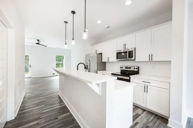an empty room with wooden floor chandelier fan and windows
