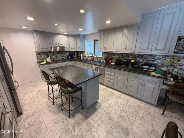 a kitchen with stainless steel appliances granite countertop a table chairs sink refrigerator and cabinets