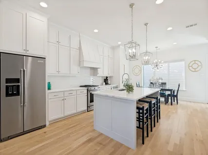 a kitchen with stainless steel appliances kitchen island granite countertop a sink a stove a refrigerator and white cabinets with wooden floor