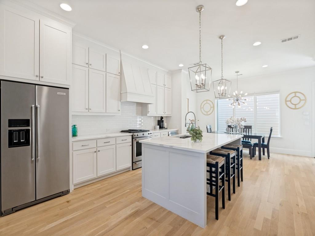 732 West 7th Street Dallas, TX 75208 - Photo 8 of 25 Gourmet kitchen featuring white shaker cabinetry, stainless steel appliances, a large center island with seating, pendant lighting, and light wood-finish flooring