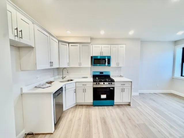 a kitchen with stainless steel appliances granite countertop a stove top oven a sink dishwasher and a refrigerator with wooden floor