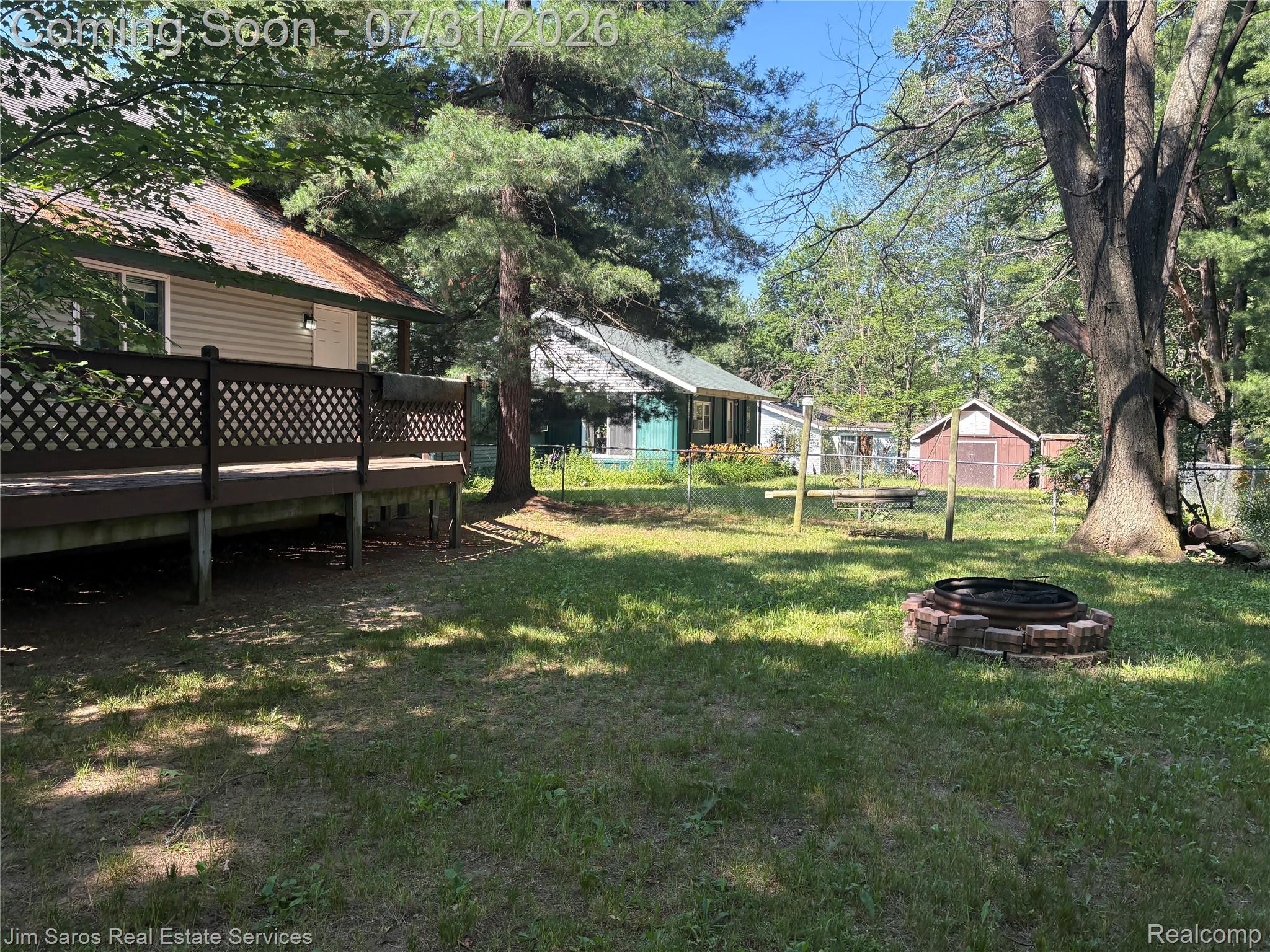 3871 Oakgrove Road Harrison, MI 48625 - Photo 2 of 12 Spacious backyard featuring a stone-ringed fire pit, mature trees, and a raised wooden deck with lattice railing