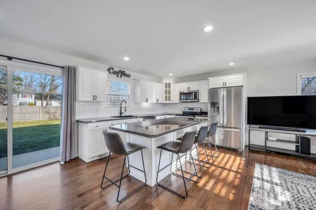 a kitchen with stainless steel appliances granite countertop a stove top oven a sink dishwasher a dining table and chairs with wooden floor