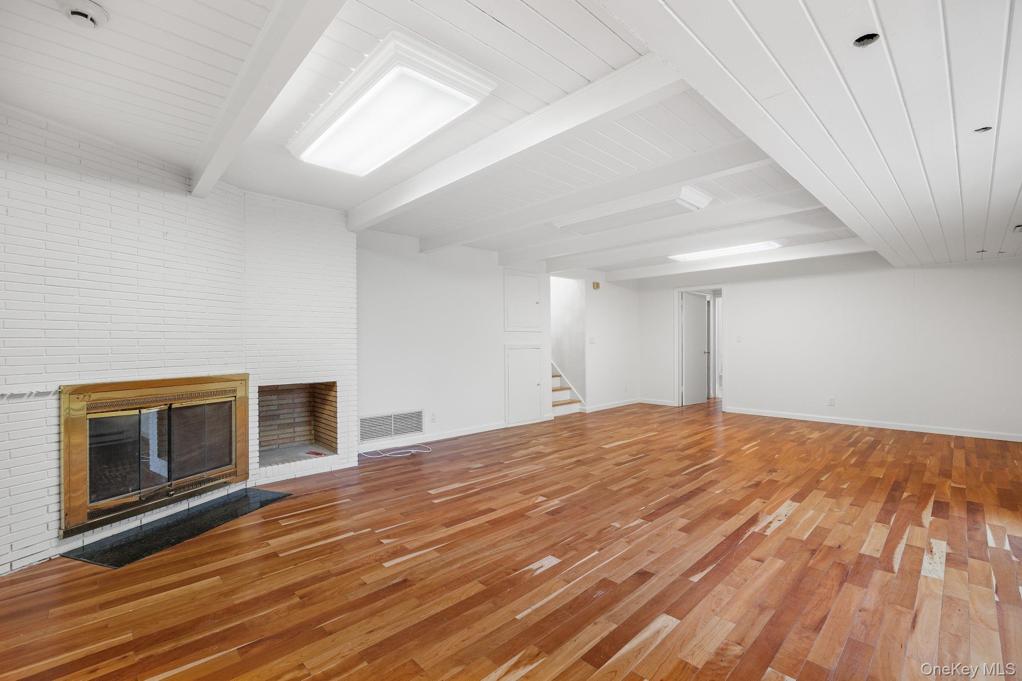 372 Heathcote Road Scarsdale, NY 10583 - Photo 17 of 20 Unfurnished living room with beam ceiling, a brick fireplace, light wood-type flooring, and stairway