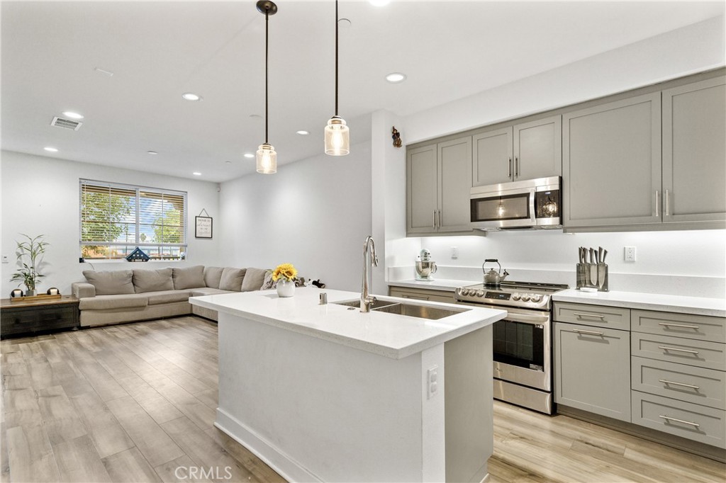 a large white kitchen with a stove a sink a dishwasher a dining table and chairs with wooden floor