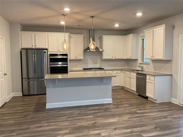 a kitchen with stainless steel appliances granite countertop a refrigerator a sink dishwasher a stove and white countertops with wooden floor