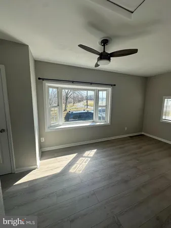 an empty room with wooden floor fan and windows