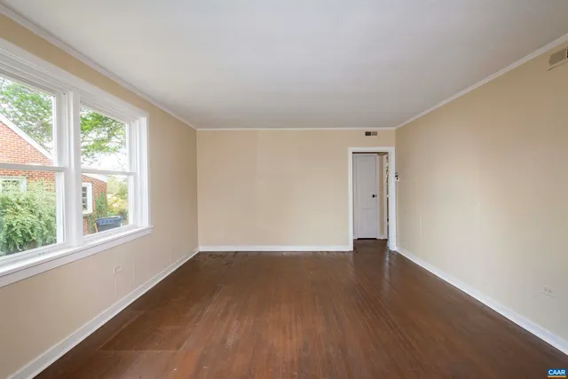 a view of an empty room with wooden floor and a window
