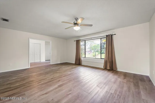 a view of an empty room with wooden floor and a window