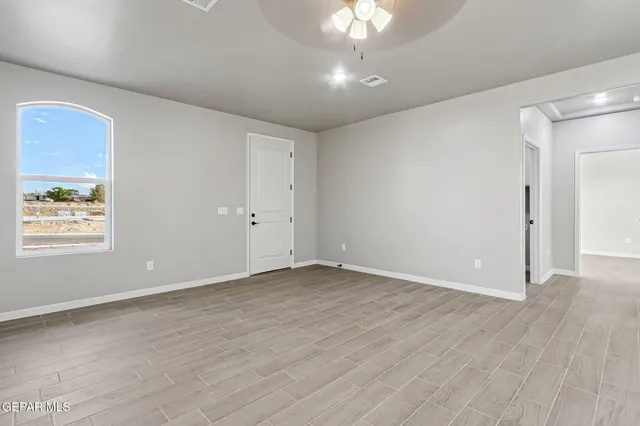 an empty room with wooden floor chandelier fan and windows