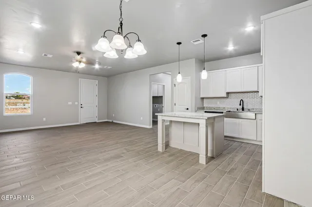 a large kitchen with granite countertop a stove a sink and white cabinets with wooden floor