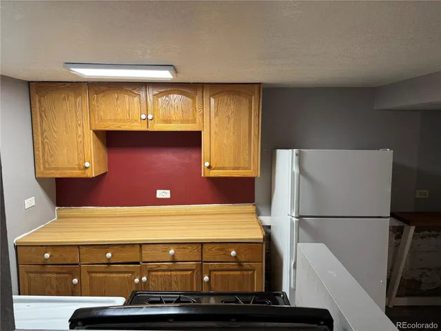 a view of an empty room with wooden floor and a kitchen