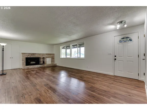 a view of an empty room with wooden floor fireplace and a window