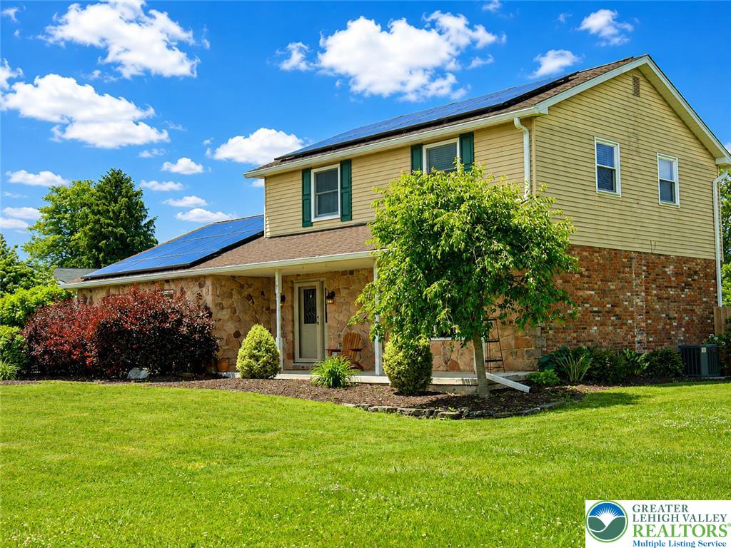 A classic two-story residence boasts solar panels, a stone facade, and verdant landscaping.