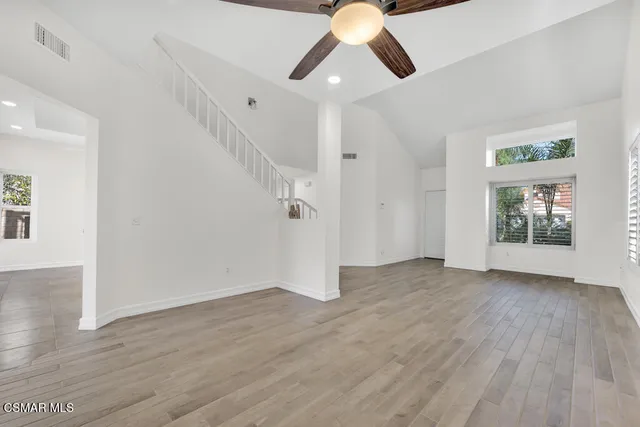 an empty room with wooden floor chandelier fan and windows