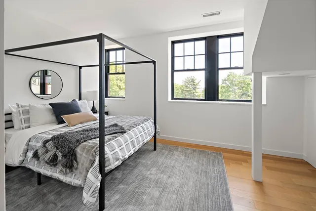 a bedroom with a bed two windows and wooden floor