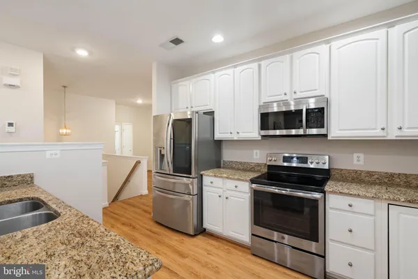 a kitchen with stainless steel appliances white cabinets a sink a stove a microwave and a refrigerator