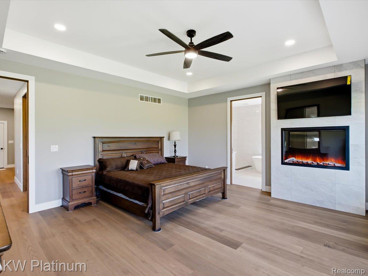 493 Wood Road Snover, MI 48472 - Photo 24 of 60 Spacious room featuring wood-finish flooring, a tray ceiling with recessed lighting and a ceiling fan, and a tiled accent wall with a built-in electric fireplace