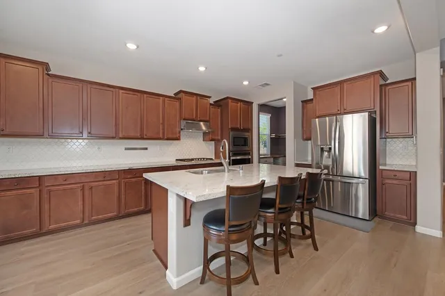 a kitchen with stainless steel appliances a table chairs refrigerator and wooden cabinets