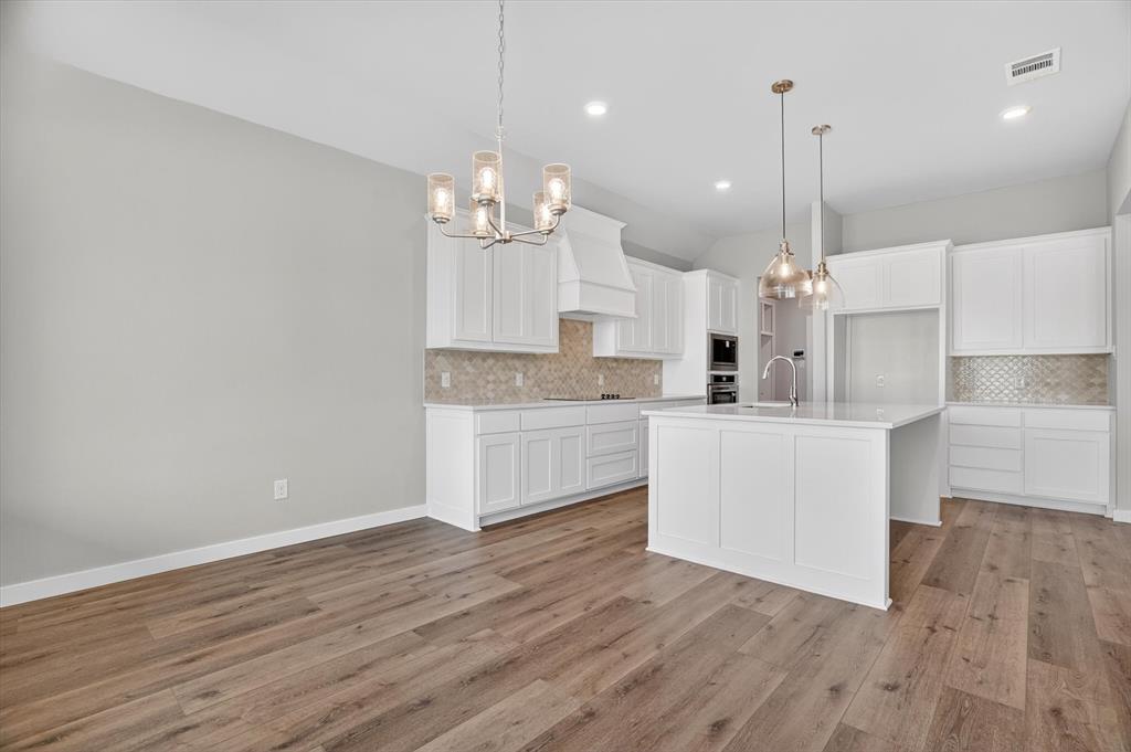 504 Clifton Court Springtown, TX 76082 - Photo 16 of 36 Open-concept kitchen and dining area featuring wood-finish flooring, white cabinetry, a kitchen island with sink, a decorative range hood, and pendant lighting