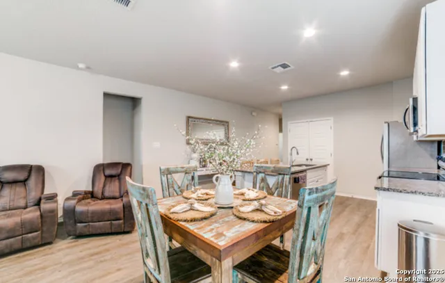 a kitchen with stainless steel appliances granite countertop a refrigerator a stove a sink a dining table and chairs with wooden floor