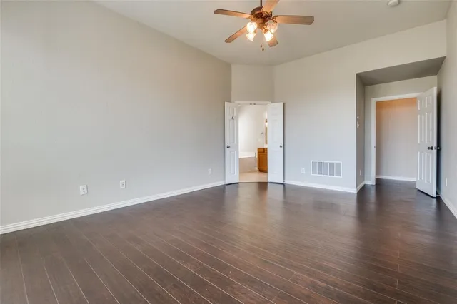 a view of an empty room with wooden floor and a ceiling fan
